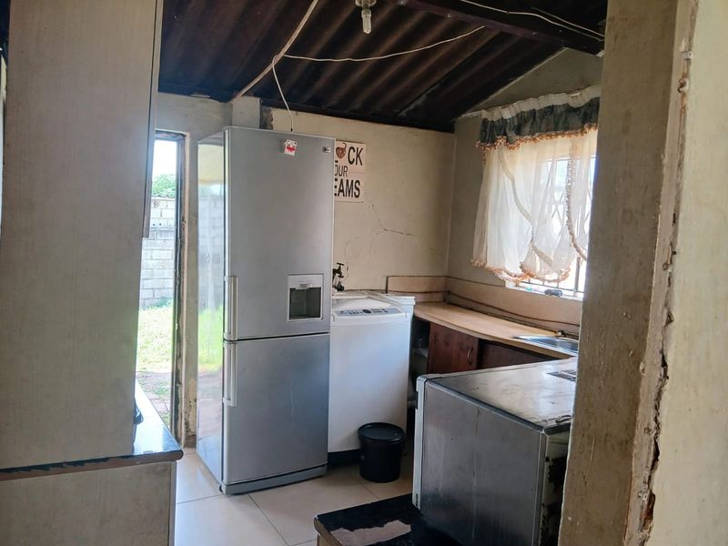 A functional kitchen area featuring basic cabinetry, a sink, and exposed roof structure, requiring significant cosmetic updates and repairs to wall finishes.