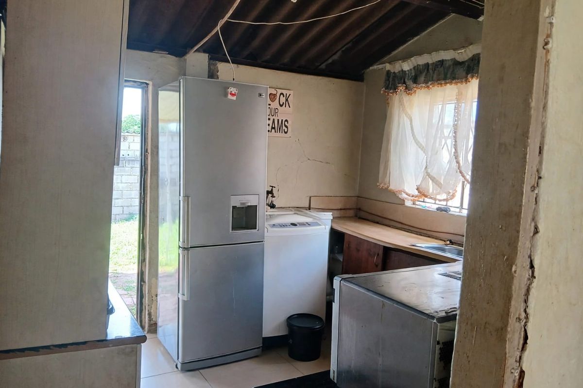 A functional kitchen area featuring basic cabinetry, a sink, and exposed roof structure, requiring significant cosmetic updates and repairs to wall finishes.