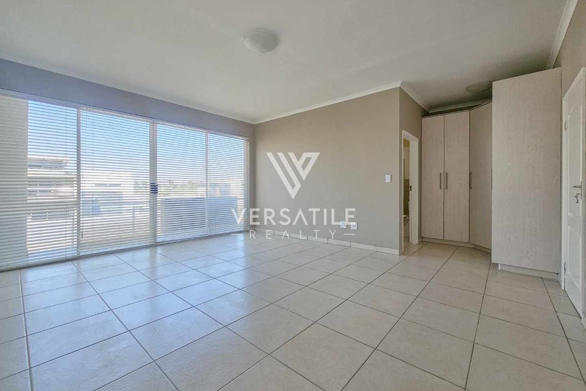 Spacious bedroom featuring neutral tiled flooring, built-in cupboards, and large sliding glass doors with venetian blinds providing ample natural light.
