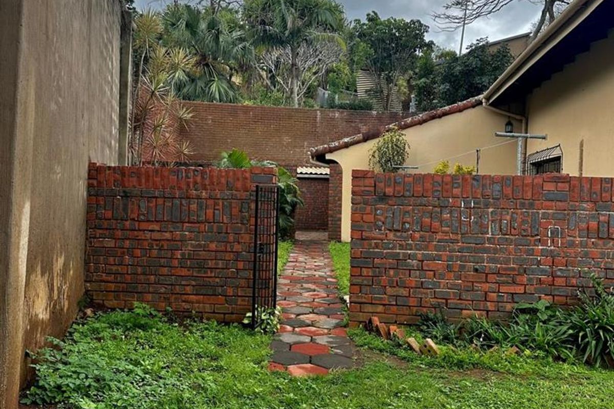 Rear garden area featuring a brick boundary wall, paved walkway, and lawn, providing access to the side of the property.