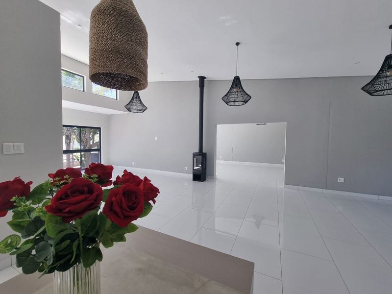 Spacious, modern living area featuring sleek white tiled floors, a contemporary freestanding fireplace, and neutral grey walls with abundant natural light.