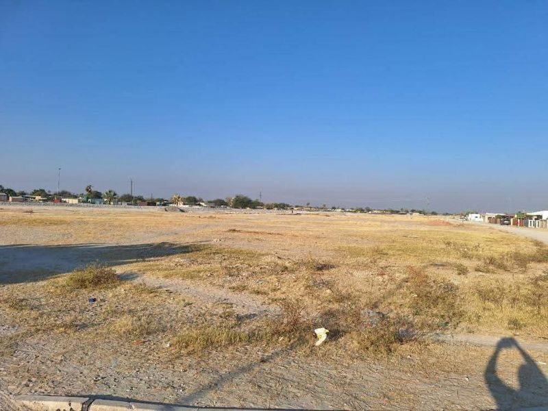 A wide-angle view of a vacant residential plot of land with dry vegetation and clear sky.