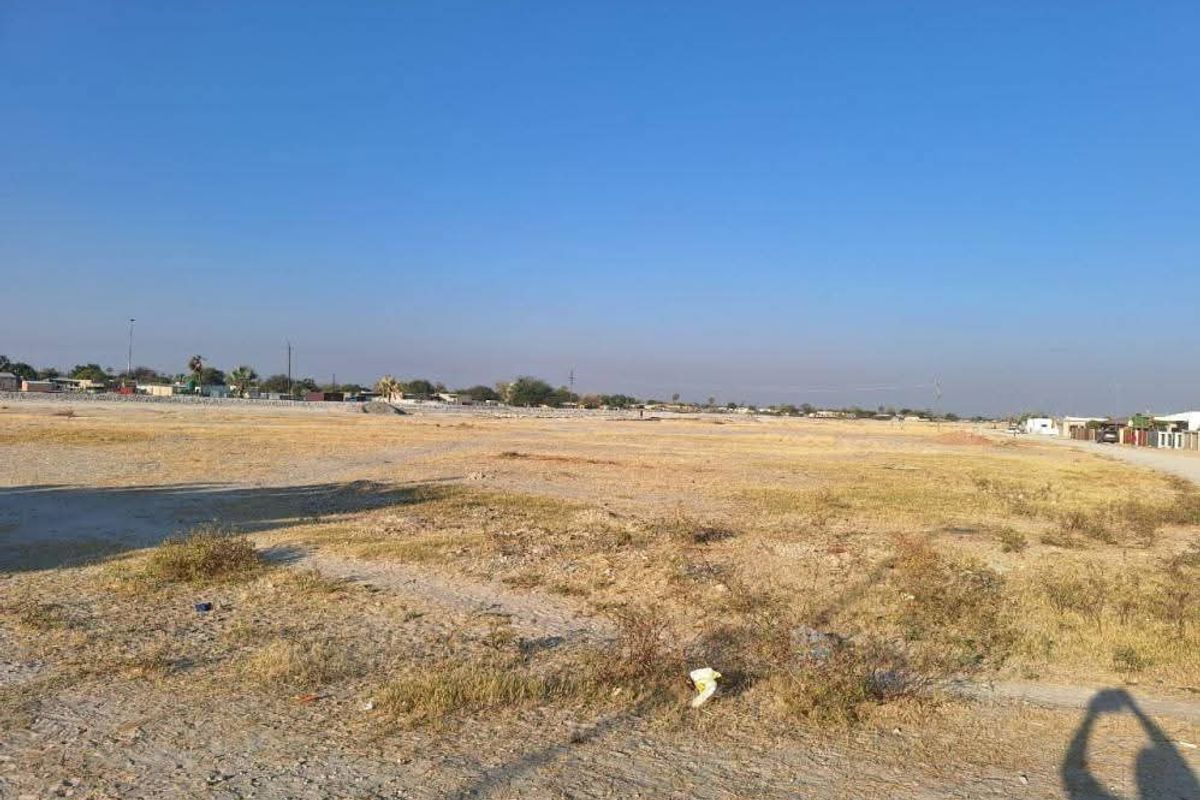 A wide-angle view of a vacant residential plot of land with dry vegetation and clear sky.
