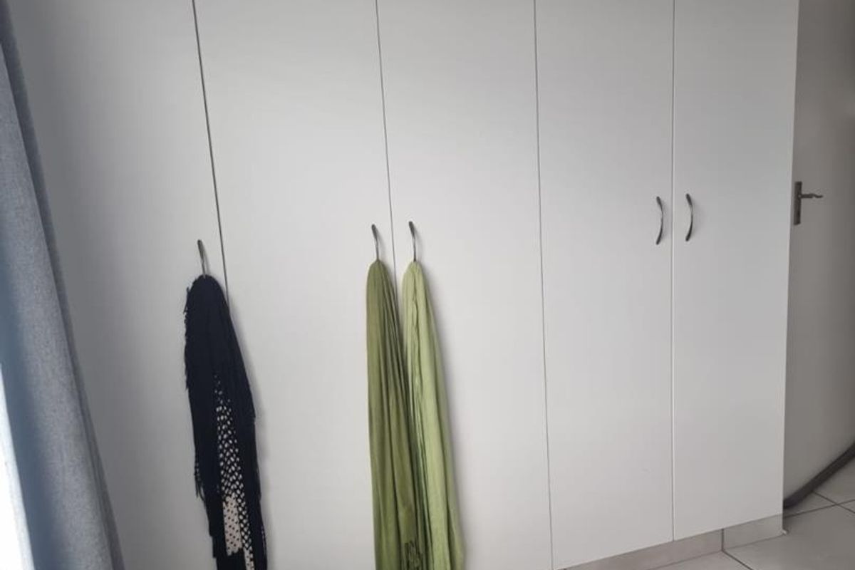 A bedroom featuring floor-to-ceiling white built-in cupboards and neutral tiled flooring.