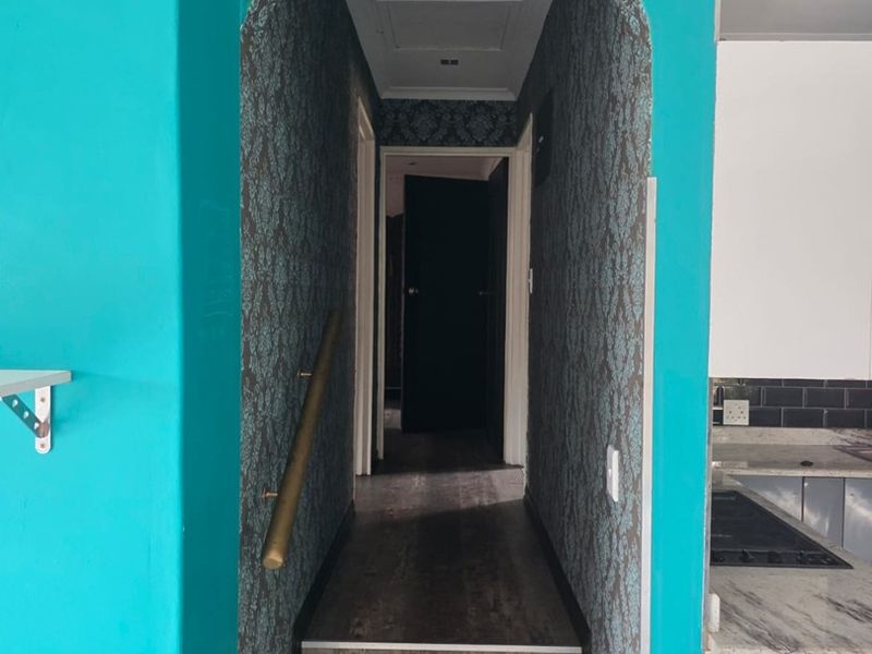 A hallway featuring an arched entryway, staircase with a handrail, and patterned wallpaper, leading to a dark interior door.