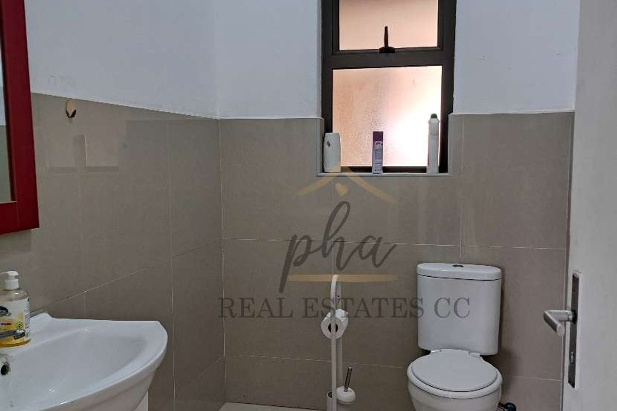 A functional bathroom featuring a vanity basin, a standard toilet, and neutral wall and floor tiling with a window for natural light.