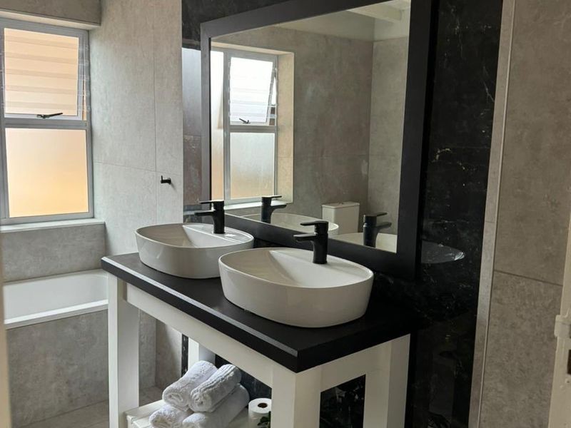 Modern bathroom featuring a double vanity with vessel sinks, black fixtures, large mirror, and neutral wall and floor tiling.