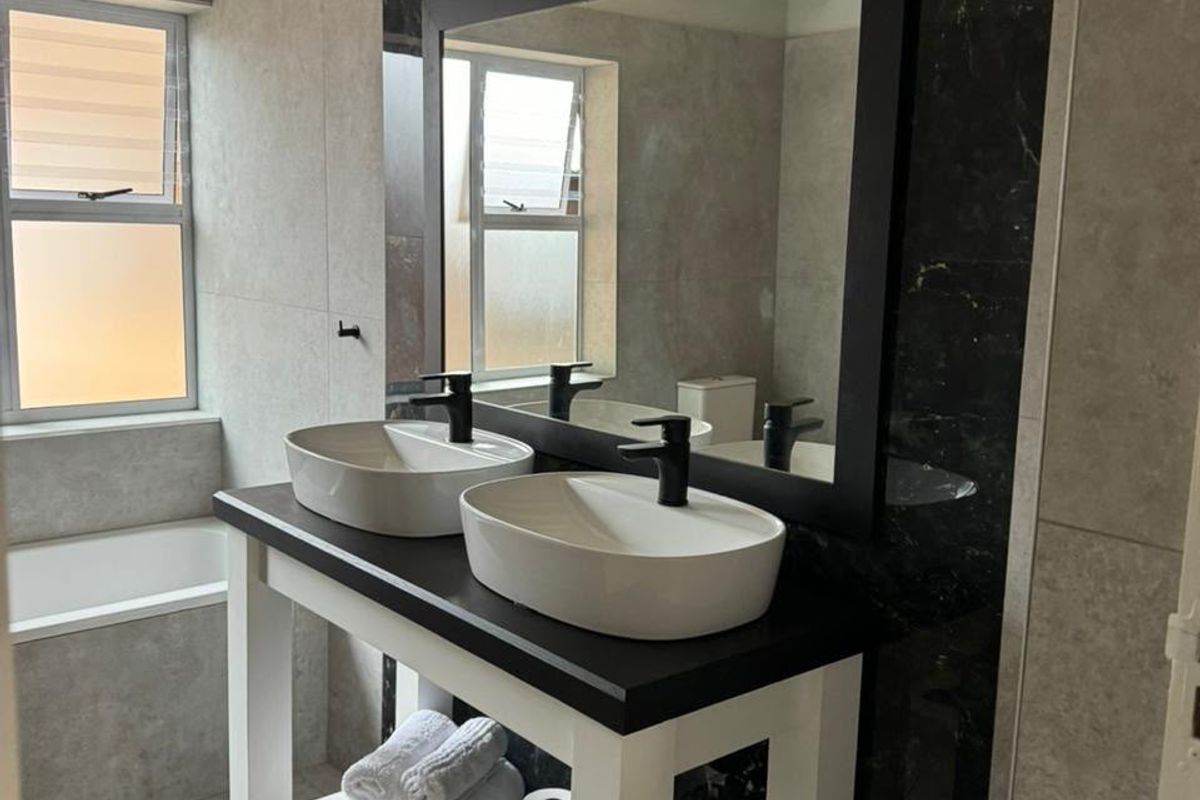 Modern bathroom featuring a double vanity with vessel sinks, black fixtures, large mirror, and neutral wall and floor tiling.