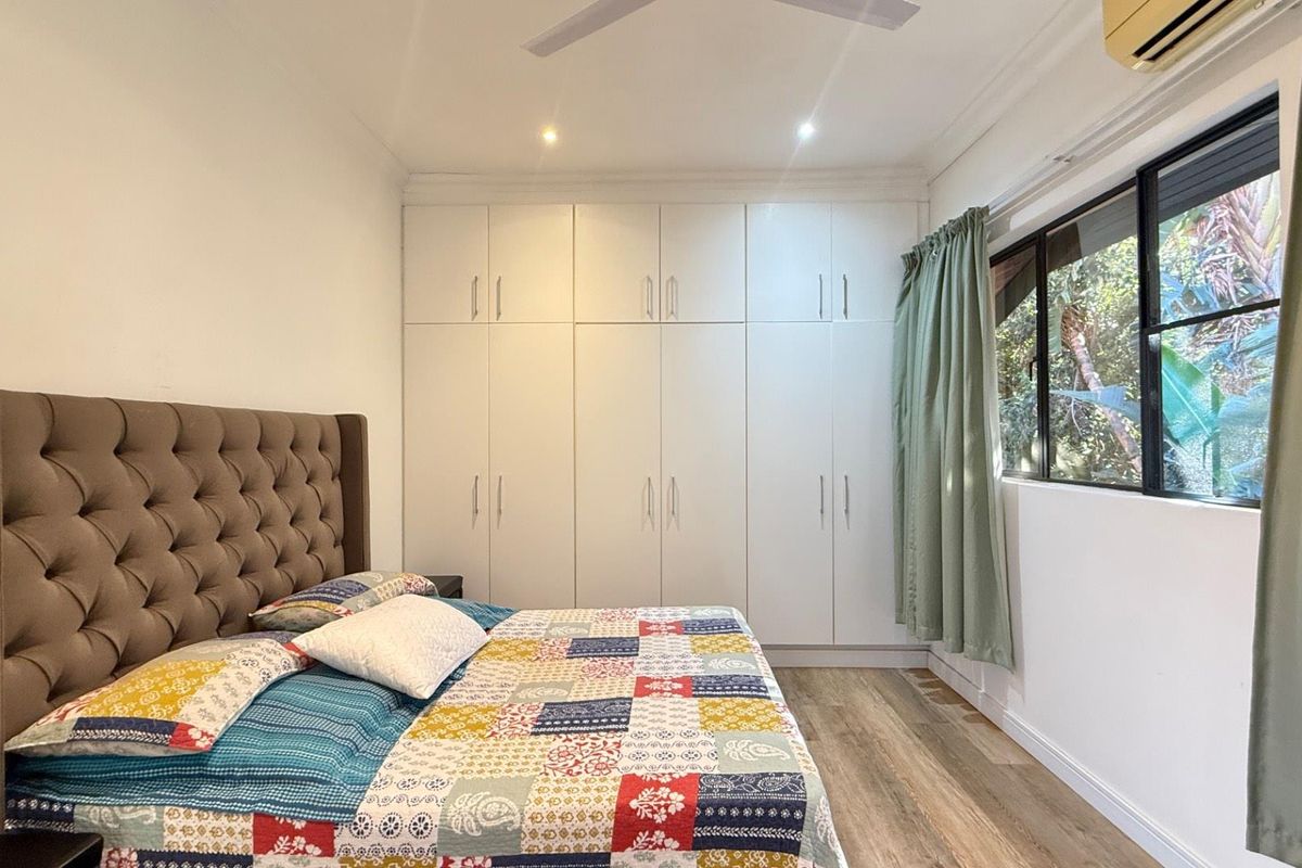 A well-maintained bedroom featuring extensive floor-to-ceiling built-in cabinetry, wood-look flooring, recessed ceiling lighting, and a wall-mounted air conditioning unit.