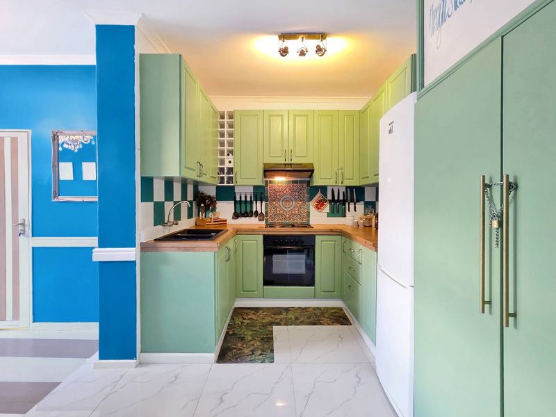 A compact, well-maintained kitchen featuring light green cabinetry, wooden countertops, a tiled backsplash, and integrated cooking appliances.