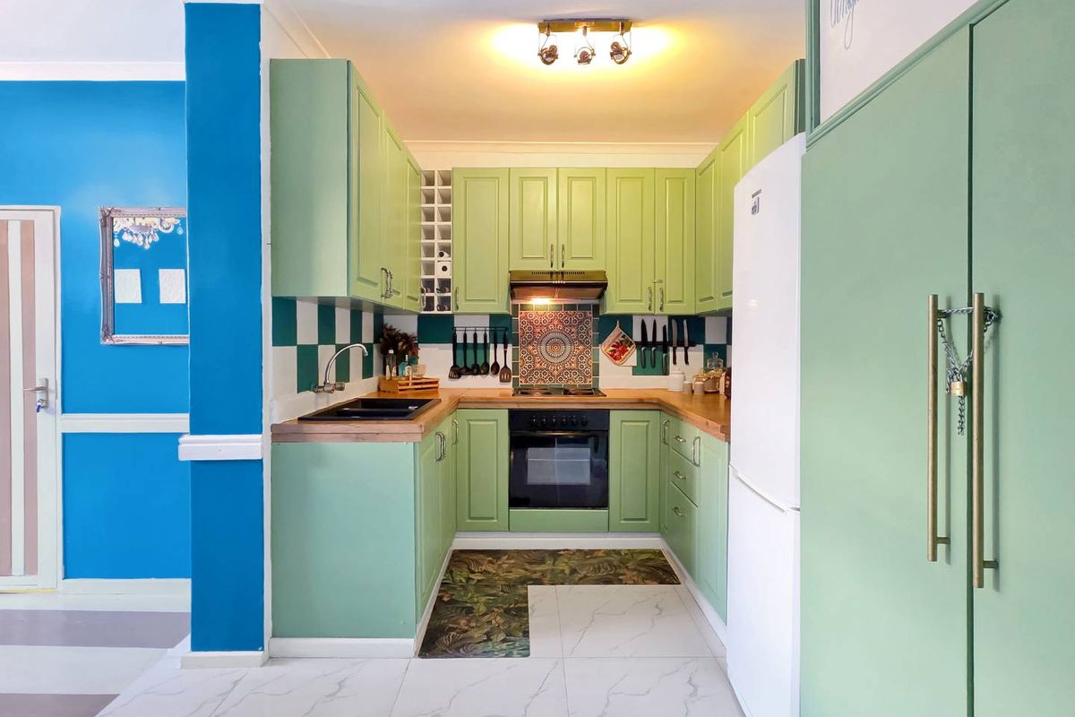 A compact, well-maintained kitchen featuring light green cabinetry, wooden countertops, a tiled backsplash, and integrated cooking appliances.