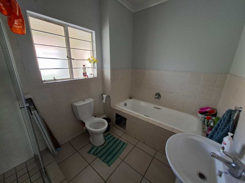 A functional bathroom featuring a bathtub, toilet, and pedestal basin with tiled finishes and natural light from a window with security bars.