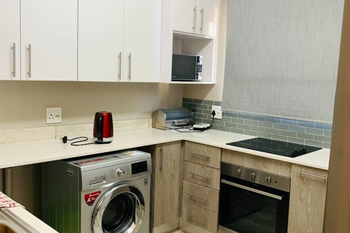Modern kitchen featuring white upper cabinets, wood-grain lower cabinetry, stone countertops, subway tile backsplash, and integrated oven and hob.