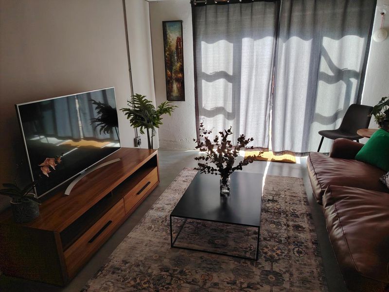 A cozy living room featuring polished concrete floors, exposed electrical conduit, and a large sliding glass door providing natural light.