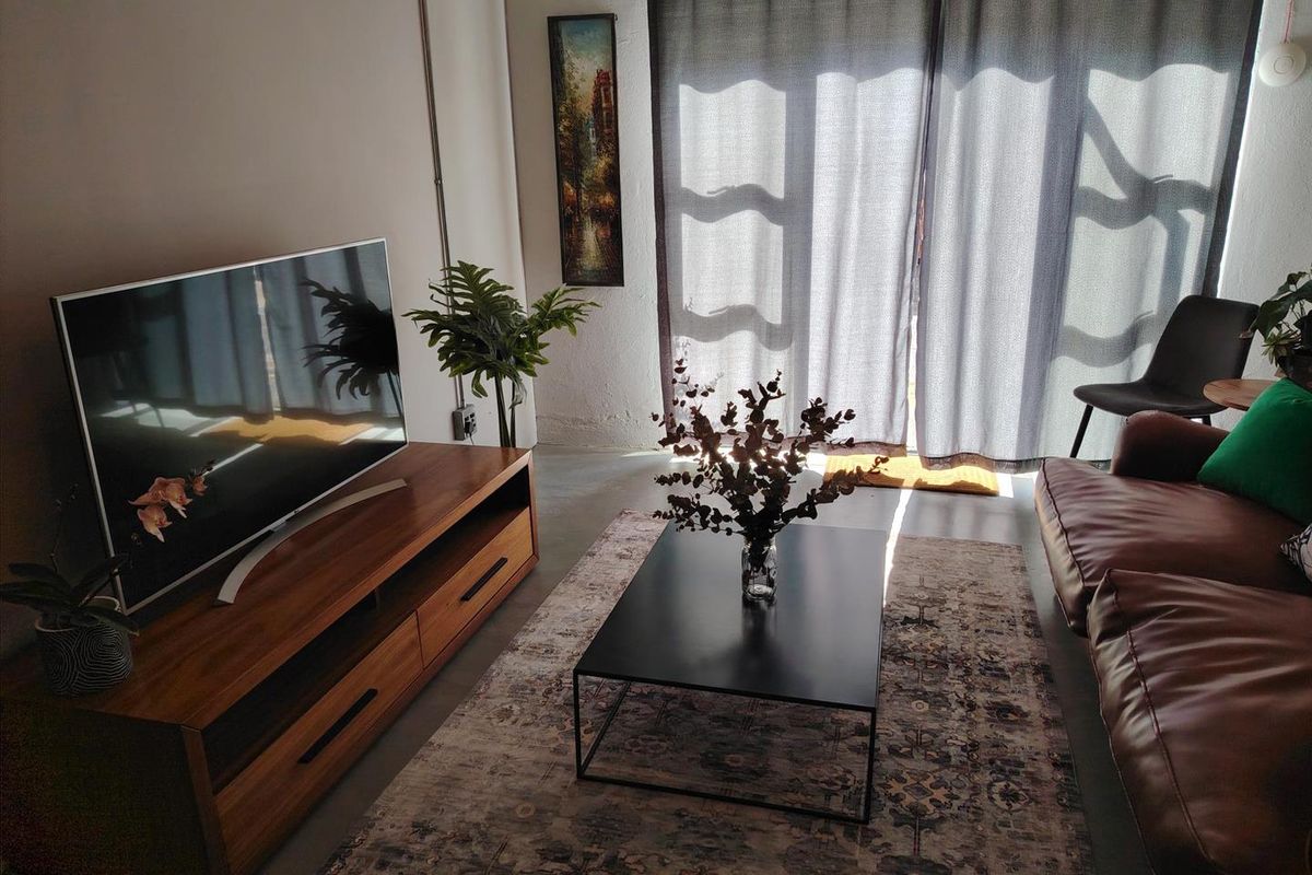 A cozy living room featuring polished concrete floors, exposed electrical conduit, and a large sliding glass door providing natural light.