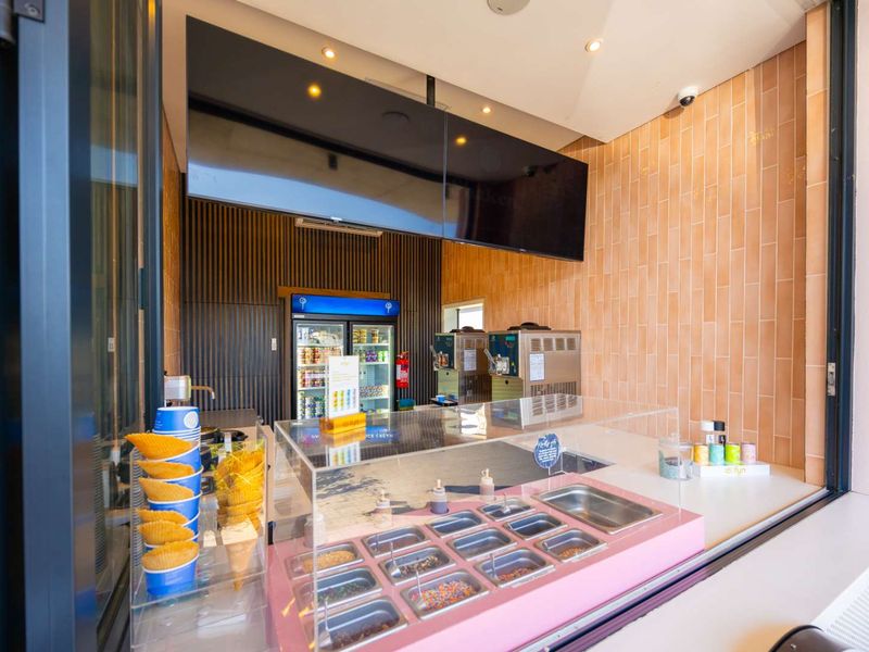 A modern, well-maintained commercial ice cream service counter featuring built-in refrigeration, soft serve machines, and stylish tiled and timber wall finishes.