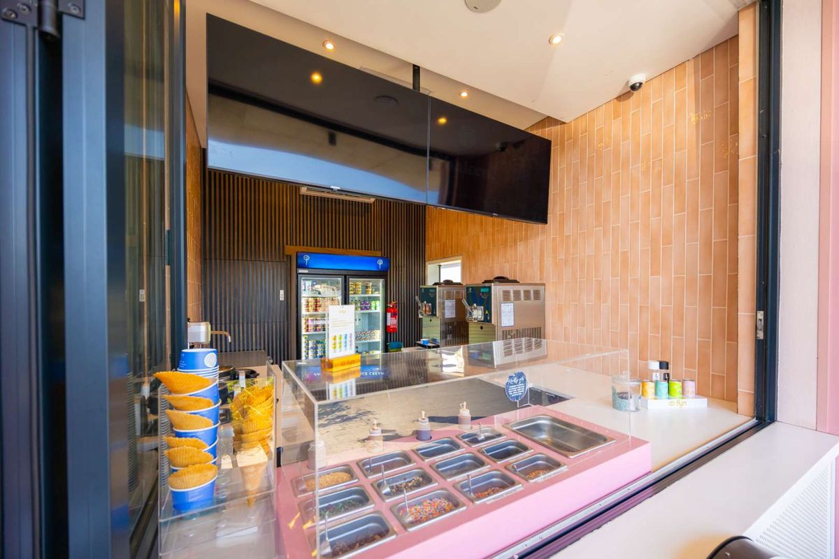 A modern, well-maintained commercial ice cream service counter featuring built-in refrigeration, soft serve machines, and stylish tiled and timber wall finishes.