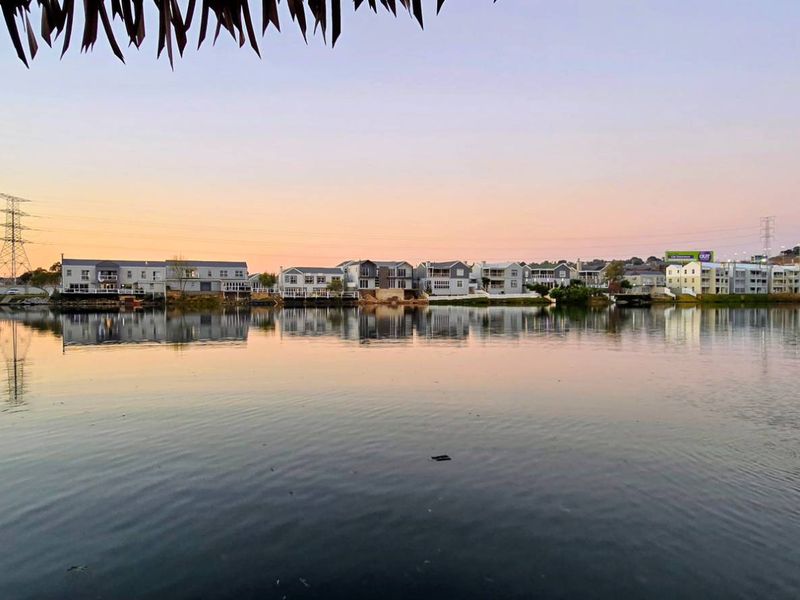 A scenic view across a calm lake towards a residential estate at sunset.