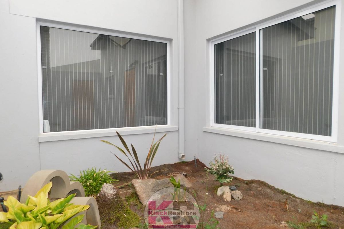 A view of a small exterior courtyard area featuring white-framed sliding windows and a compact garden bed.