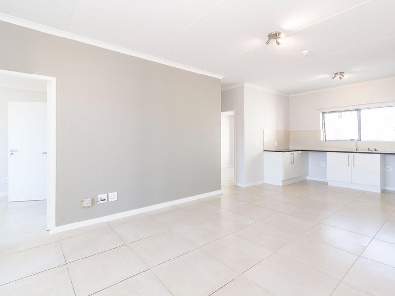 Spacious open-plan living area featuring neutral tiled flooring, a modern kitchen with built-in cabinetry, and clean, well-maintained finishes throughout.