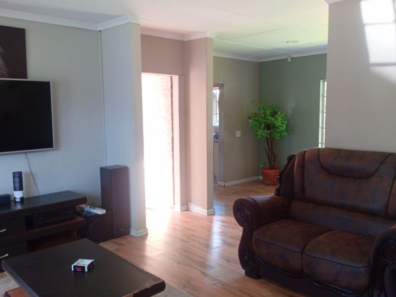 A living room featuring laminate flooring and neutral wall tones, with an open layout leading to an adjacent space.