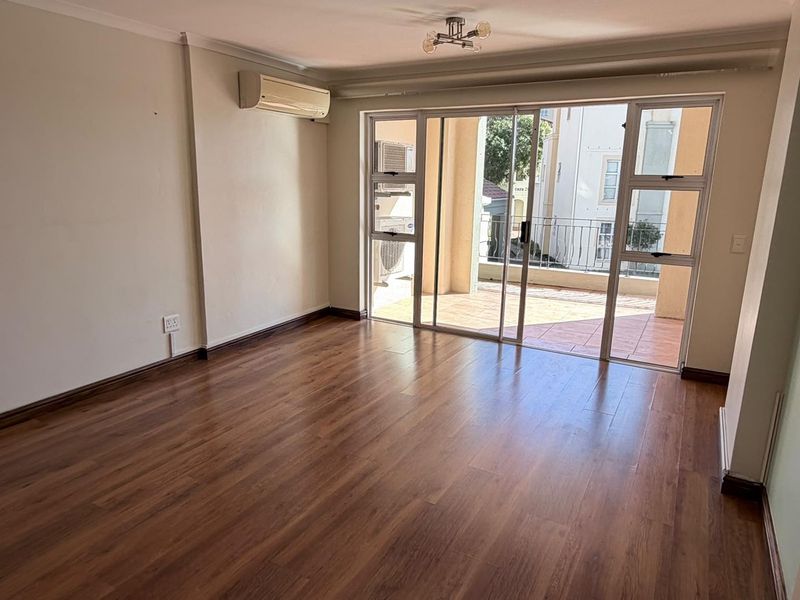 Spacious, empty living area featuring laminate flooring, a split-system air conditioner, and large sliding glass doors leading to an outdoor balcony.
