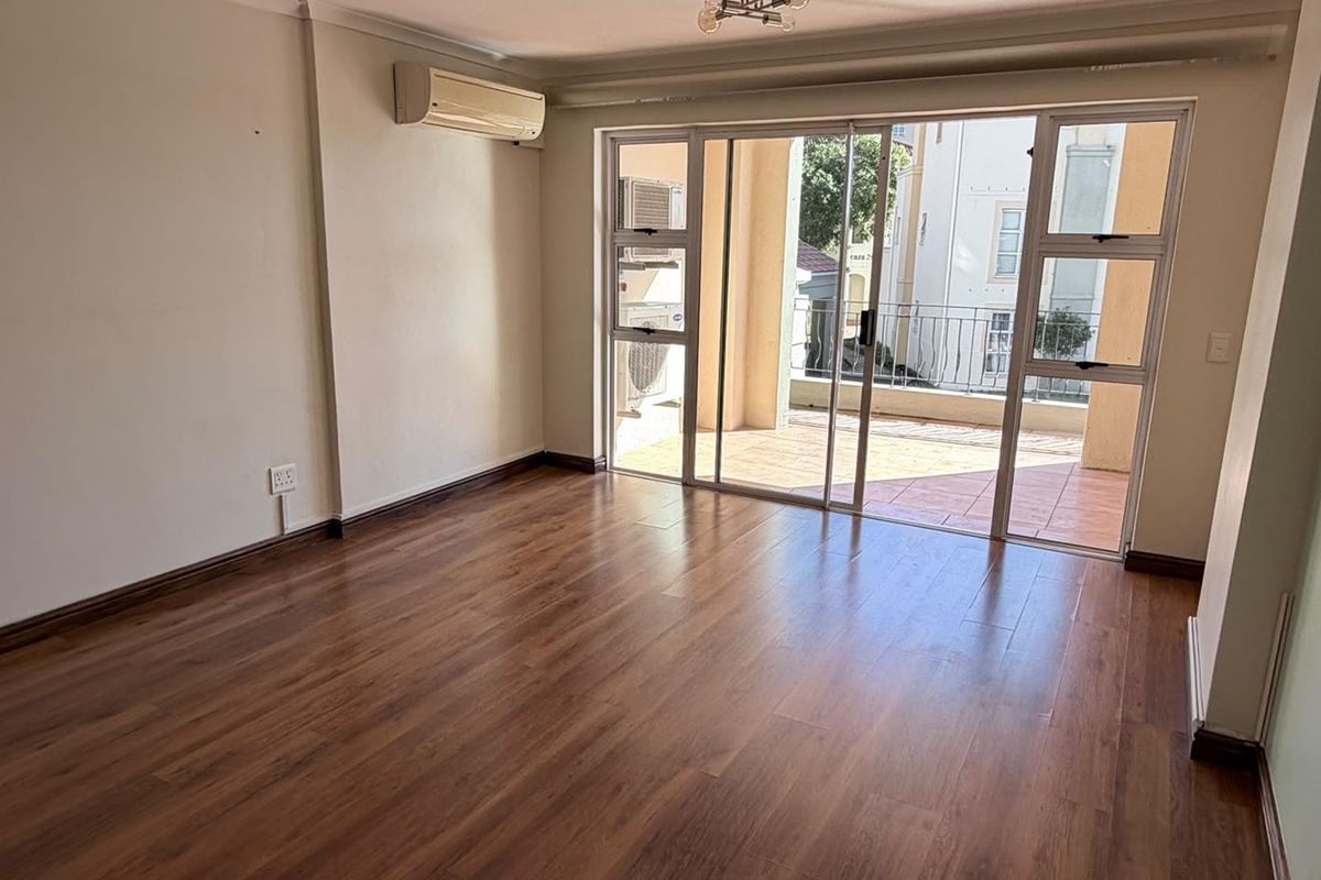 Spacious, empty living area featuring laminate flooring, a split-system air conditioner, and large sliding glass doors leading to an outdoor balcony.