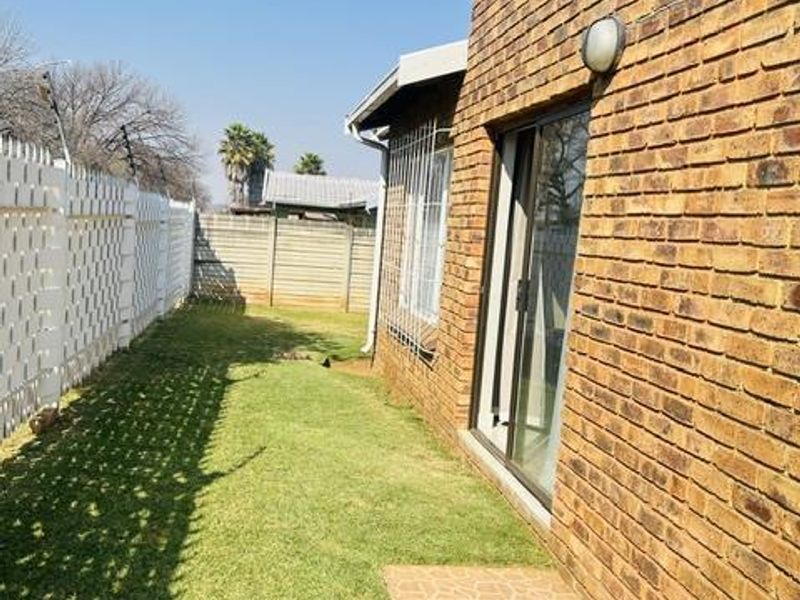 Rear exterior view of the house featuring a face brick facade, sliding glass door, small tiled patio area, and a private lawn with perimeter fencing.
