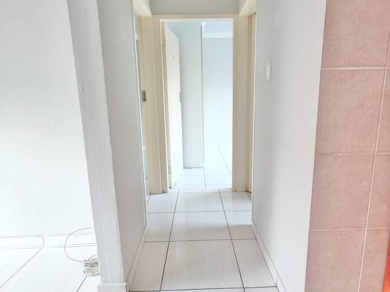 A vacant hallway featuring white tiled flooring and neutral walls, providing access to adjacent rooms within the townhouse.