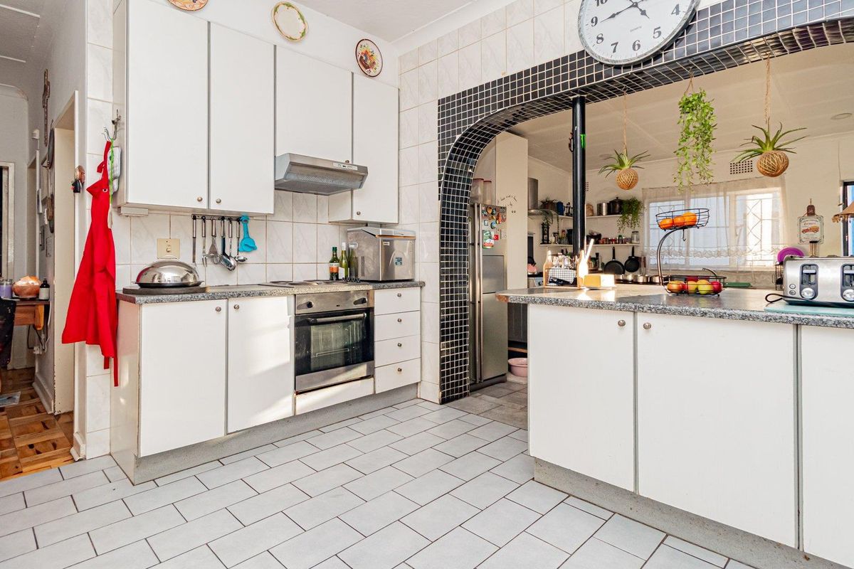 A functional kitchen featuring white cabinetry, stone countertops, tiled flooring, and a distinctive tiled archway connecting to an adjacent space.