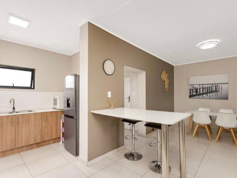 A modern open-plan kitchen and dining area featuring wood-finish cabinetry, a breakfast bar, and neutral tiled flooring throughout.