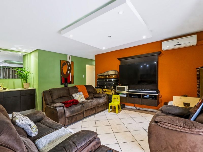 A living room featuring a recessed ceiling detail, tiled flooring, a built-in media console, and a wall-mounted split-system air conditioner.