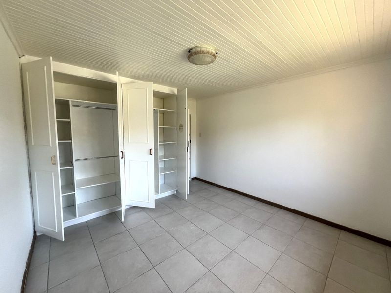 A clean, empty bedroom featuring tiled flooring, a beadboard ceiling, and ample built-in cupboard storage space.