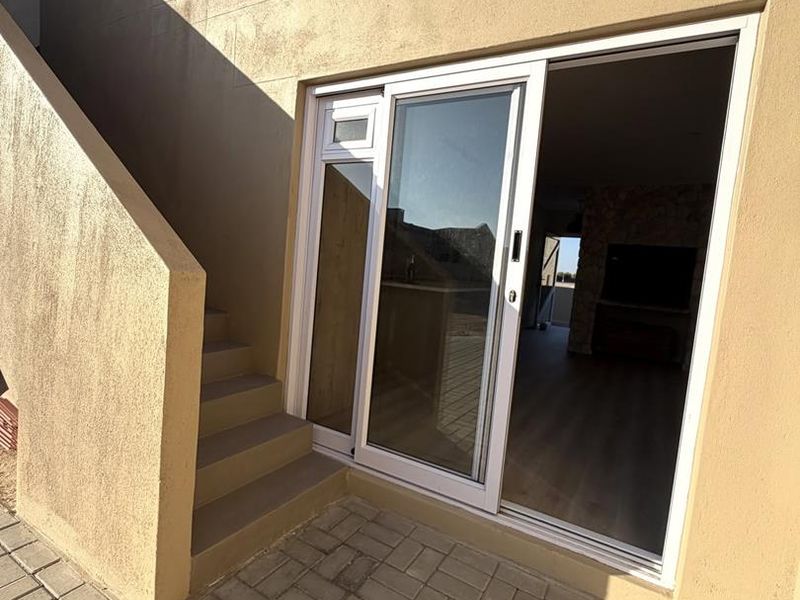Rear exterior view showing a paved patio area, concrete staircase, and sliding glass door access to the interior living space.