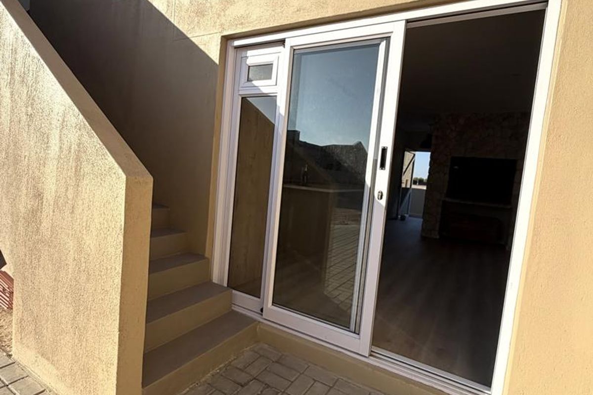 Rear exterior view showing a paved patio area, concrete staircase, and sliding glass door access to the interior living space.