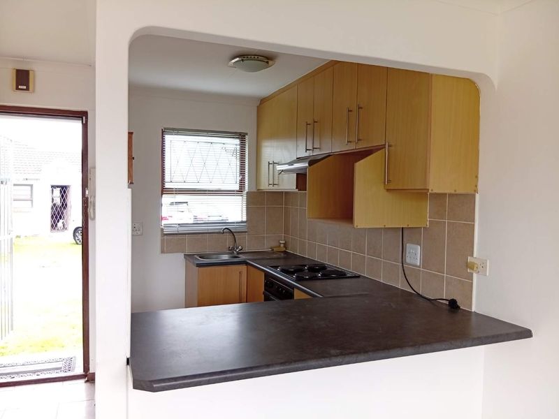 Compact kitchen featuring laminate cabinetry, dark countertops, built-in hob, and tiled splashback, with an open-plan layout and direct access to the exterior.