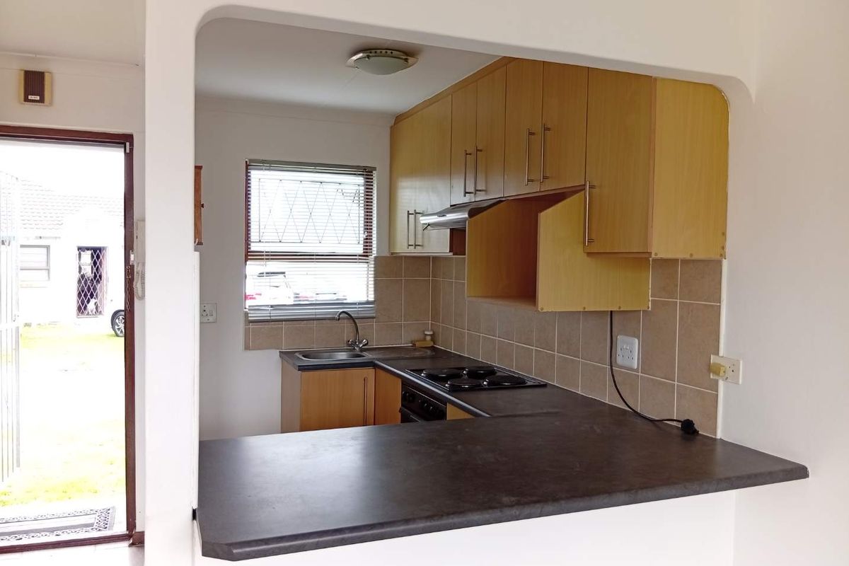 Compact kitchen featuring laminate cabinetry, dark countertops, built-in hob, and tiled splashback, with an open-plan layout and direct access to the exterior.