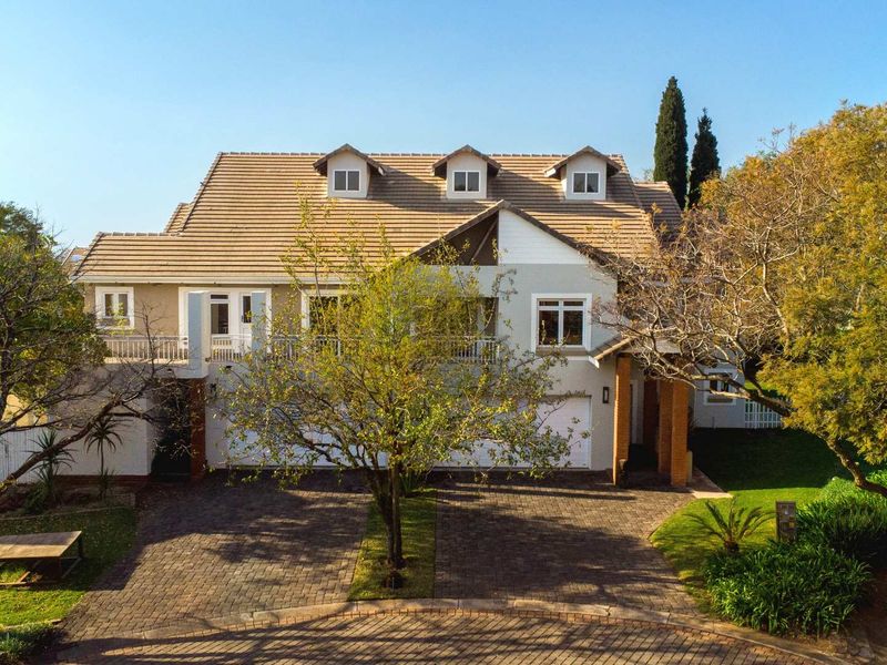 A well-maintained double-story residential property featuring a tiled roof, dormer windows, a spacious paved driveway, and an integrated double garage.