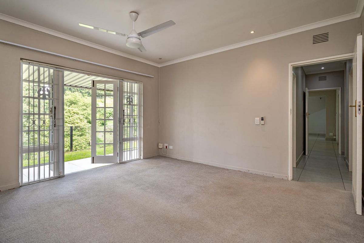 Spacious, empty living room featuring neutral carpeting, a ceiling fan, and direct access to an outdoor patio through a secure sliding glass door.