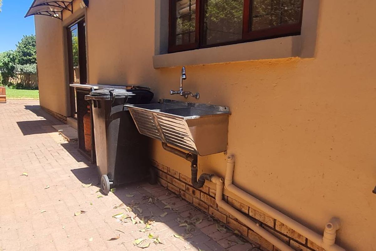 Rear exterior area featuring a paved patio, a wall-mounted stainless steel wash trough, and external plumbing fixtures.