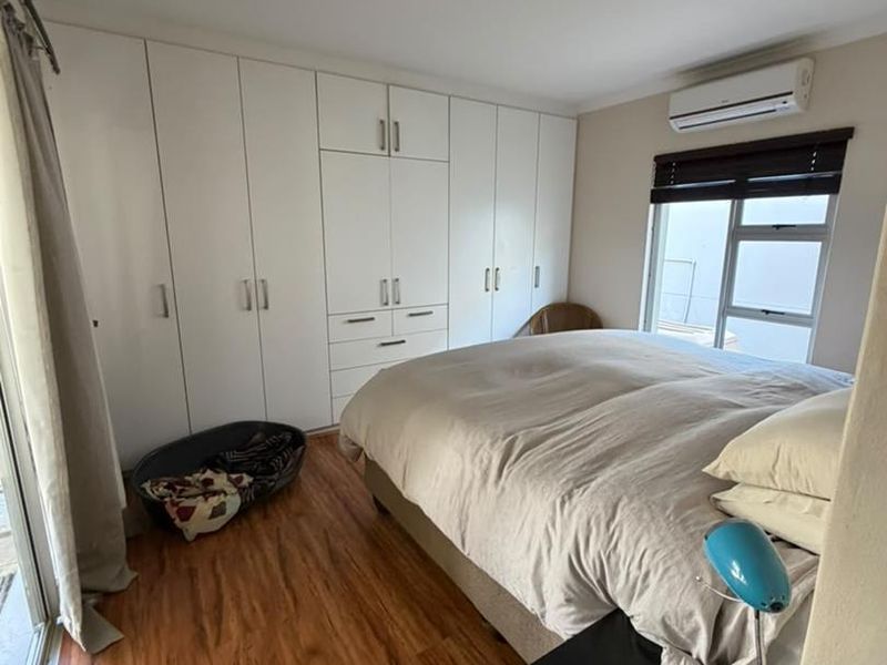 A well-lit bedroom featuring extensive built-in cupboards, laminate flooring, and a wall-mounted air conditioning unit with access to an outdoor area.