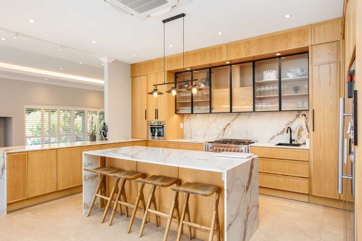 Modern kitchen featuring light wood cabinetry, marble countertops and backsplash, a central island, and high-end integrated appliances with recessed lighting.