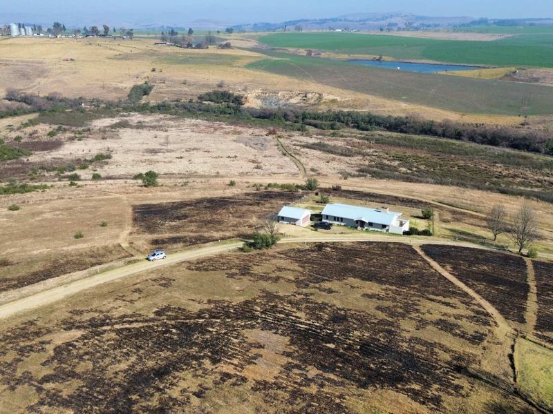 Aerial view of a residential property situated on a large expanse of rural land with a gravel driveway and surrounding open fields.