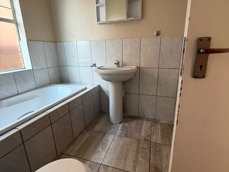 A functional bathroom featuring a pedestal basin, built-in bathtub, and toilet with neutral wall and floor tiling.