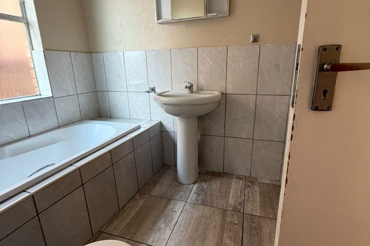 A functional bathroom featuring a pedestal basin, built-in bathtub, and toilet with neutral wall and floor tiling.