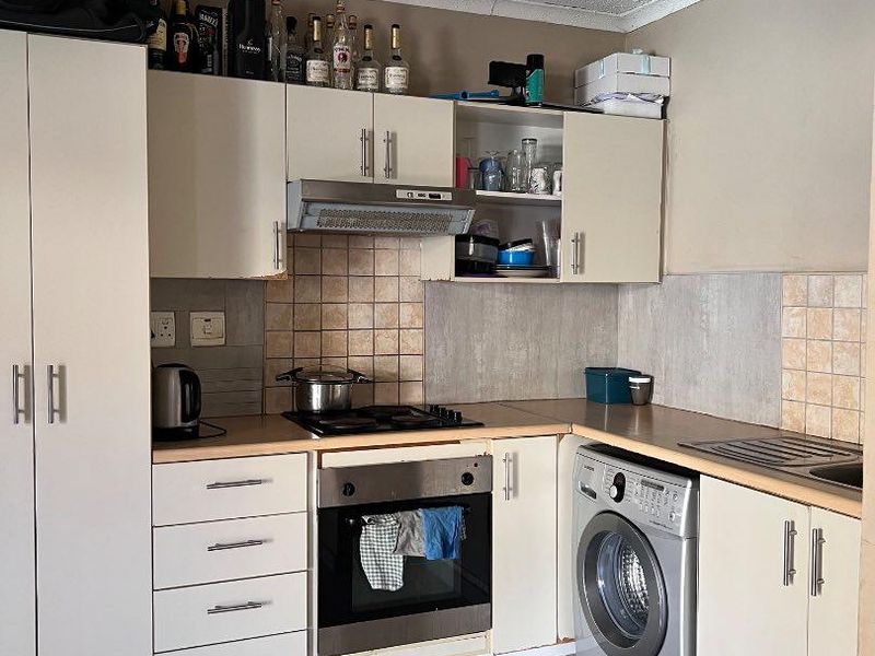 A functional kitchen featuring built-in cabinetry, laminate countertops, a gas hob with extractor, and integrated space for a washing machine.