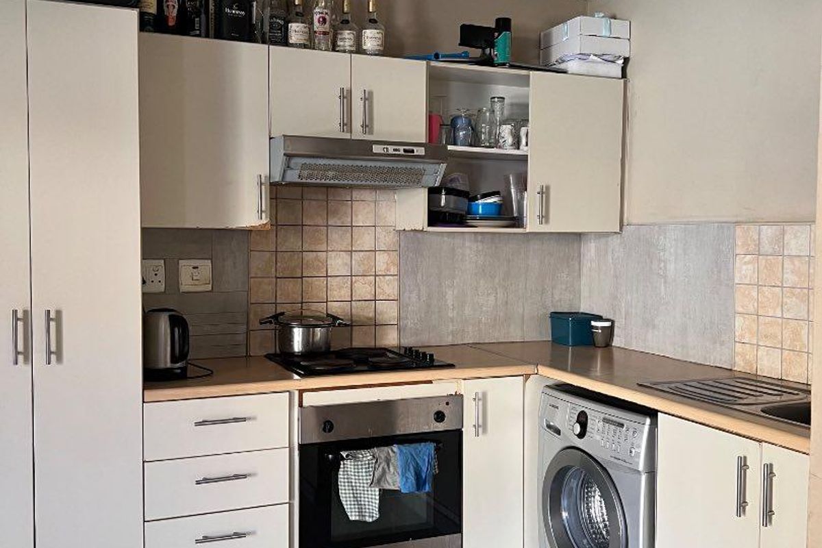 A functional kitchen featuring built-in cabinetry, laminate countertops, a gas hob with extractor, and integrated space for a washing machine.