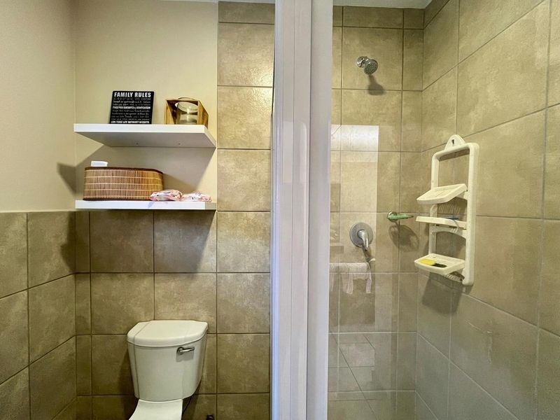 A functional bathroom featuring a tiled shower enclosure, a standard toilet, and wall-mounted floating shelves for storage.