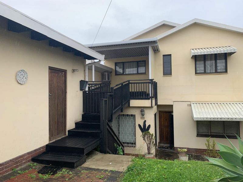 Rear exterior view of the property featuring a timber staircase leading to an upper balcony, with security bars and metal awnings on windows.