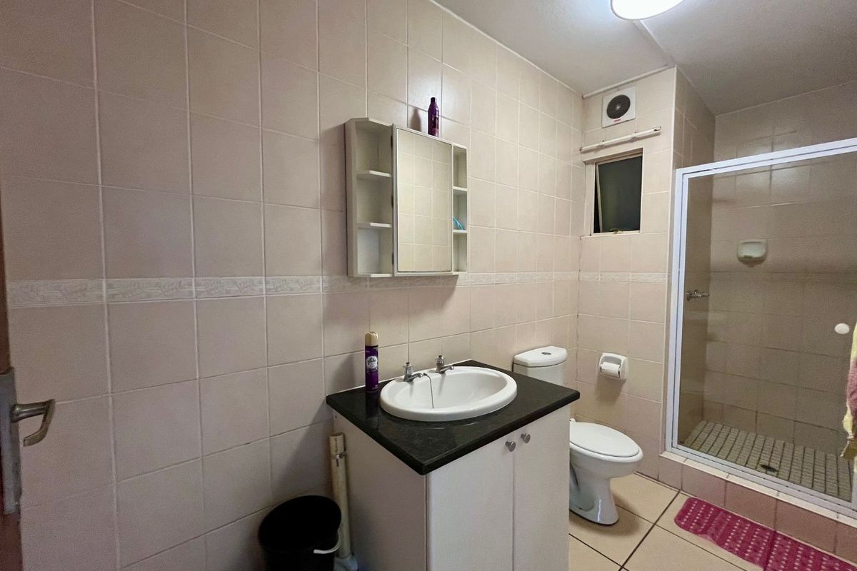 A functional bathroom featuring a vanity with a stone countertop, a glass-enclosed shower, and neutral wall tiling.